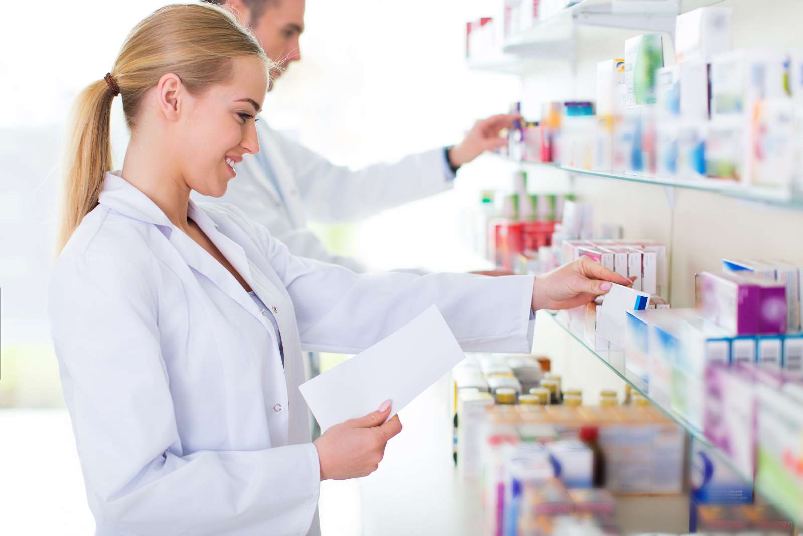 Apotherkerin und Apotheker suchen Medikamente in einem Regal
