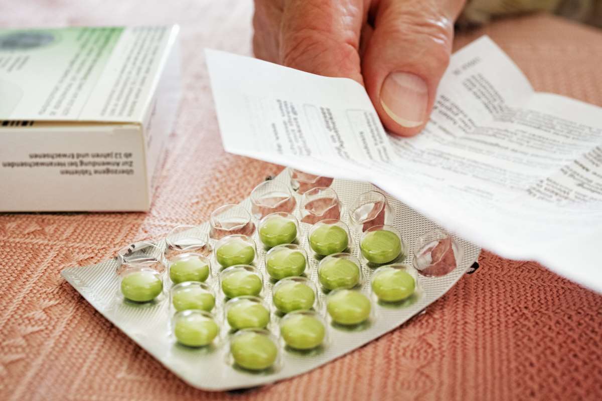 Eine Packung mit Medizin und eine Hand, die einen Beilegezettel  hält